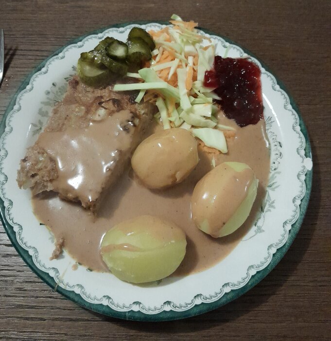 Traditionell måltid: köttfärslimpa, potatis, brun sås, lingonsylt, inlagda gurkor, råkostsallad, på dekorerad tallrik.