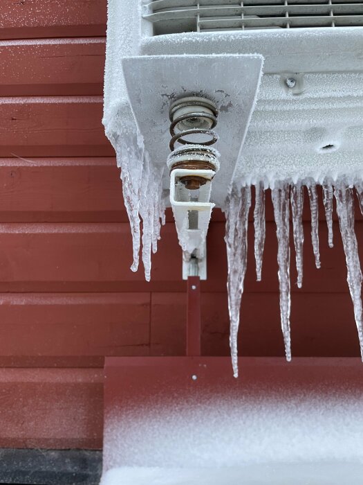 Utomhuslampa täckt av frost och isbildningar med istappar hängande nedåt mot en snötäckt yta.