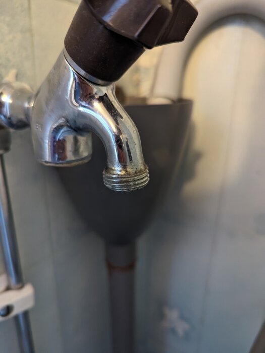 Närbild på kromad kran med vattenfläckar och kalkavlagringar, svart duschhandtag, bakgrund av badrumsinteriör.