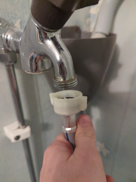 En hand håller en avtagen duschmunstycket framför kranen i ett badrum.