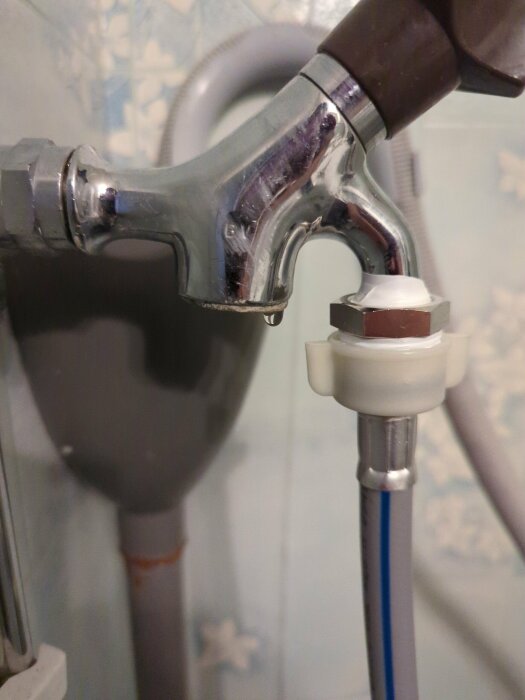 Kromad kran med påmonterad vattenbesparande anordning och blå slang i ett badrum.