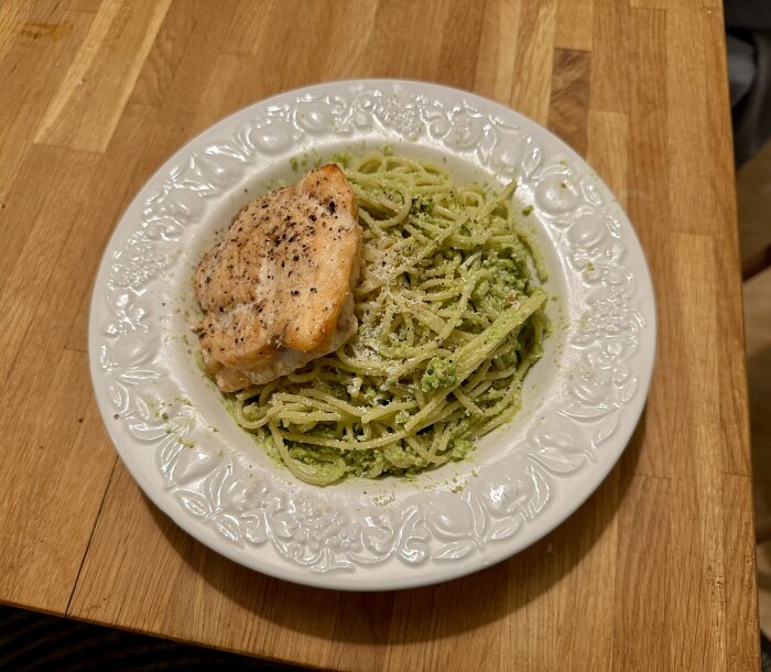 Ett fat pasta med pesto och grillad kyckling, serverat på ett dekorativt vitt fat.