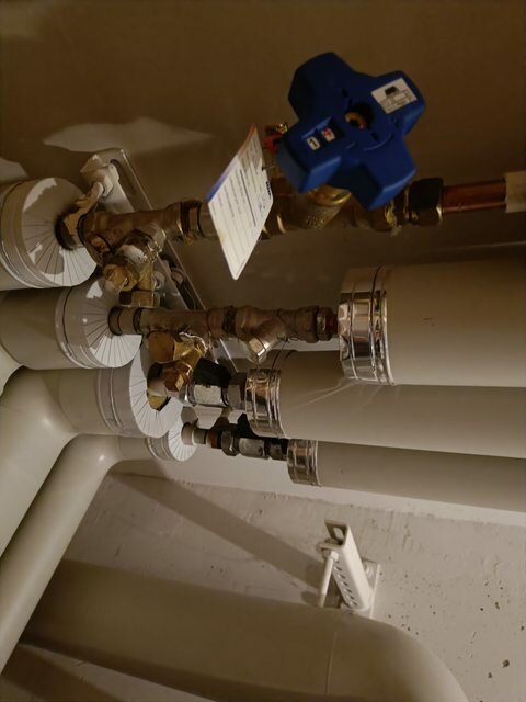VVS-installation med vattenrör, ventiler och kopplingar mot en vit vägg.