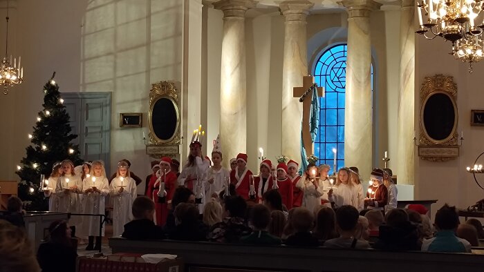 Barn i luciatåg med ljus och tomtekläder inne i kyrka. Julstämning, sång, traditionellt evenemang, Sverige.