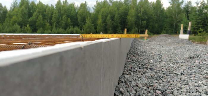 Mätmeter på armerade betongplintar vid byggarbetsplats, grus, skog i bakgrunden.