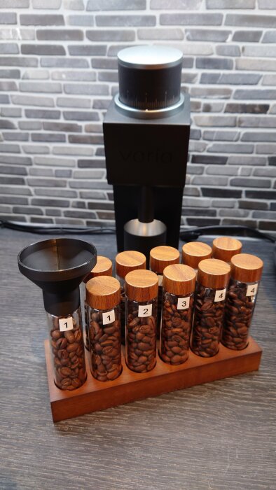 Kaffebönor i numrerade burkar, kaffekvarn, filterhållare, träbricka, tegelvägg i bakgrunden.