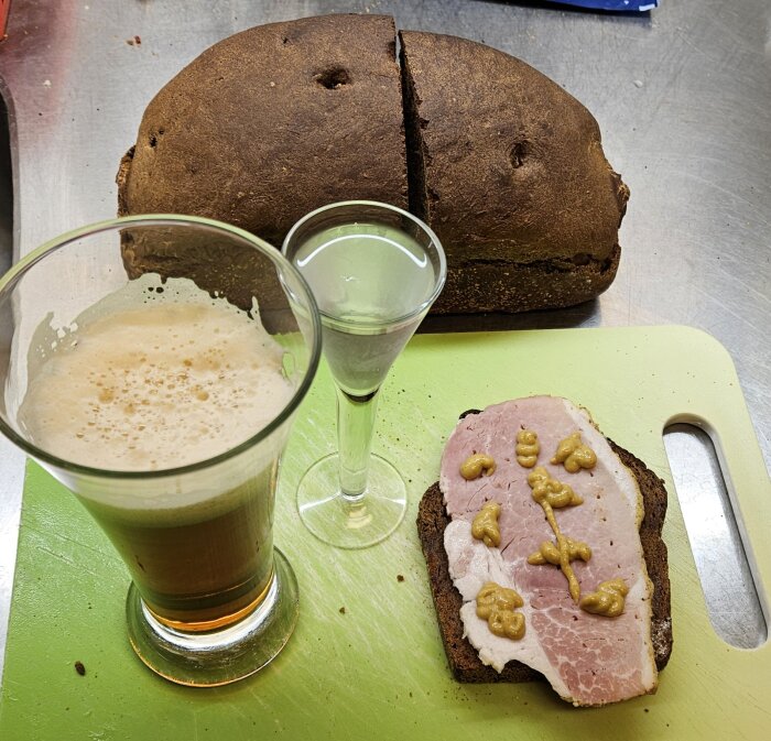 Mörkt bröd, halverat, ölglas, snaps, skärbräda, smörgås med skinka och senap.