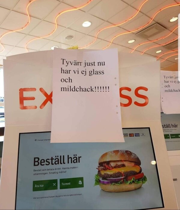 Skylt på restaurang informerar att glass och mjukdricka är slut, framför digital beställningsskärm.