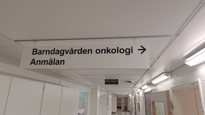 Sjukhuskorridor med skylt för Barnonkologi och Anmälan, belysning, dörrar och informationstavlor.