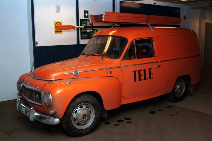 Gammal orange bil med "TELE"-text, steger på taket, parkerad inomhus, retro, nostalgisk, klassisk design.
