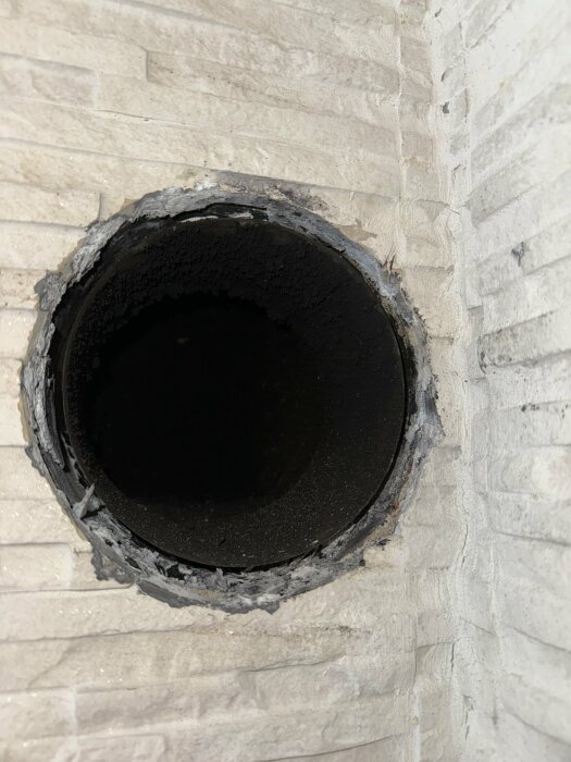 Runt hål genom murad vägg; antydan av isolering eller tätning; potentiell kanal för installation.