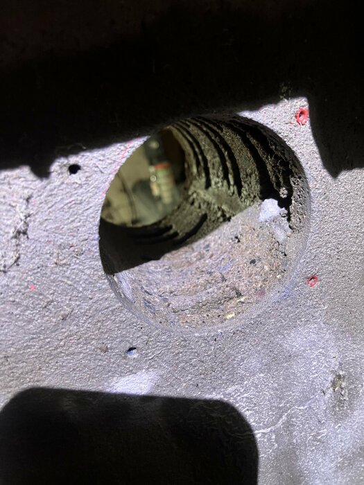 Close-up av ett runt, ihåligt objekt med koncentriska cirklar, troligen en borrning i betong, något synligt genom hålet.