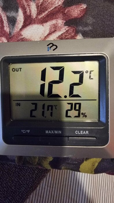 Digital termometer visar inomhus och utomhustemperatur samt inomhusfuktighet. 21,7°C inne, 12,2°F ute, 29% fuktighet.