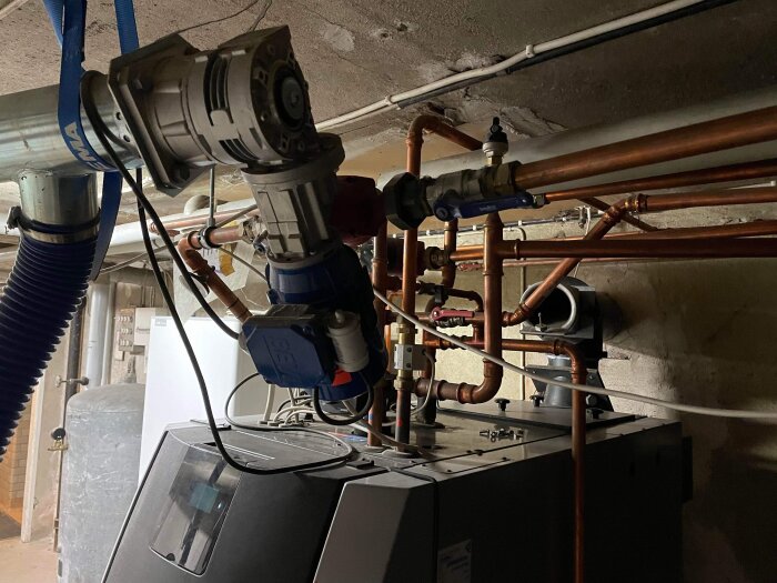Ett pannrum med kopparledningar, fläktar och värmesystemutrustning i en källare.