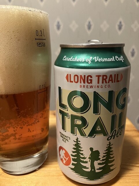 Ölglas med skum bredvid en Long Trail Ale burk. Träunderlag, diskret bakgrund.