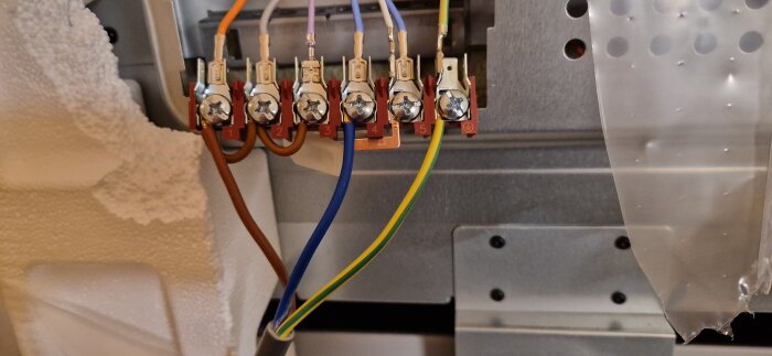 Elektrisk anslutning med färgkodade kablar och numrerade terminaler inne i en apparat.