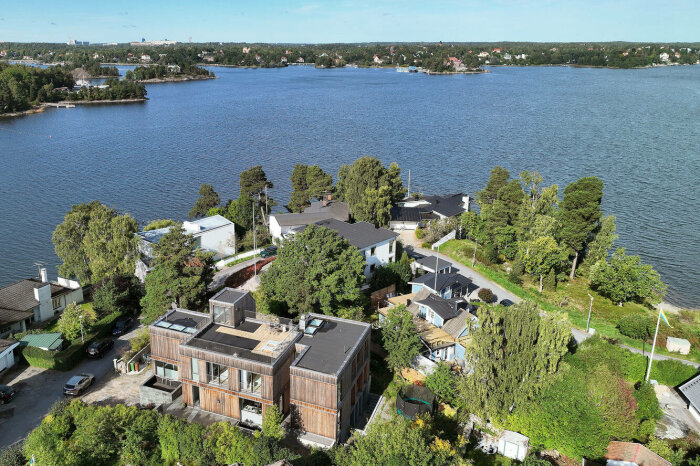 Luftvy av ett villaområde vid vatten, med blandning av moderna och traditionella hus, grönska och bilar.