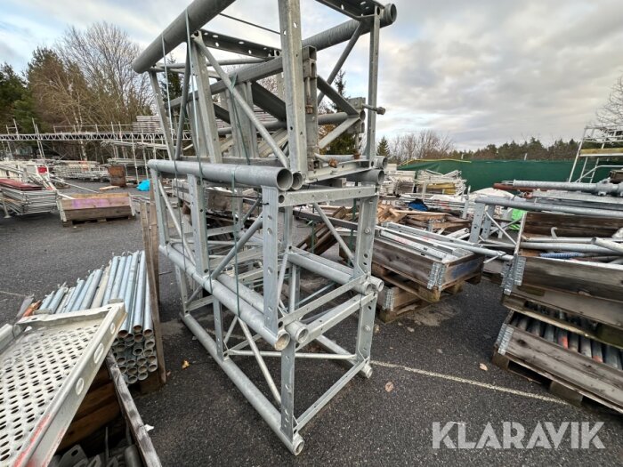 Ställningsdelar och byggnadsmaterial staplade utomhus på asfalterad mark.