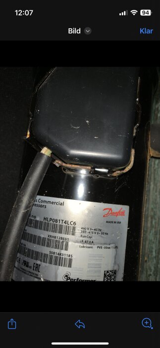 Närbild på en sliten svart apparat med betraktade skador, etikett från Danfoss, elektriska specifikationer synliga.