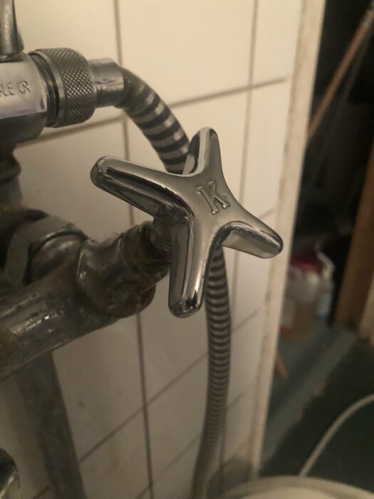 Kran med stjärnformad vred märkt med "K", troligen för kallt vatten, silverfärgad mot kakelvägg.