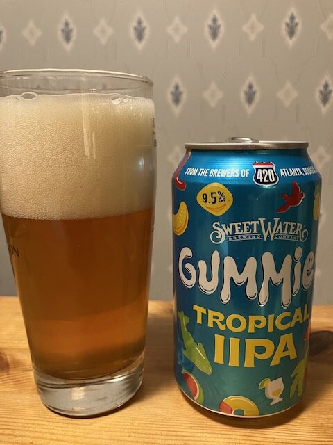 Ett glas med öl och en ölburk med texten "SweetWater Gummie Tropical IIPA" mot tapetbakgrund.