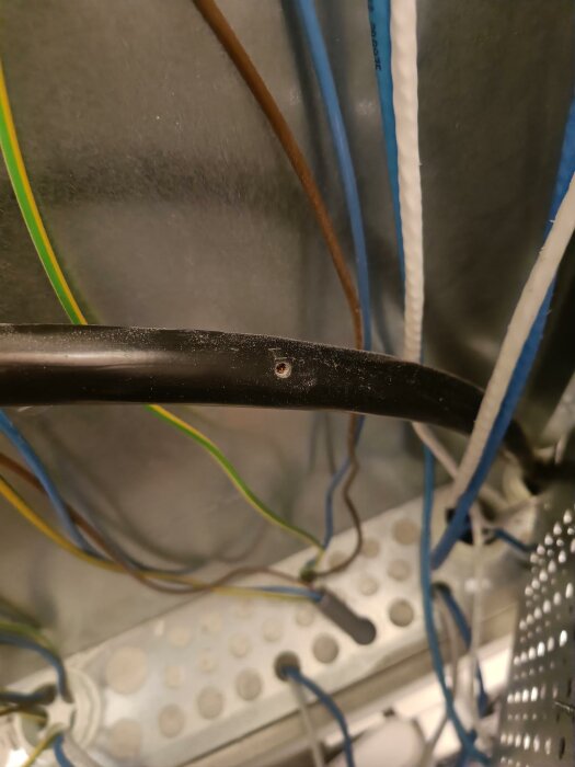 En svart kabel med skada och trådar exponerade, mot bakgrund av andra kablar och utrustning.
