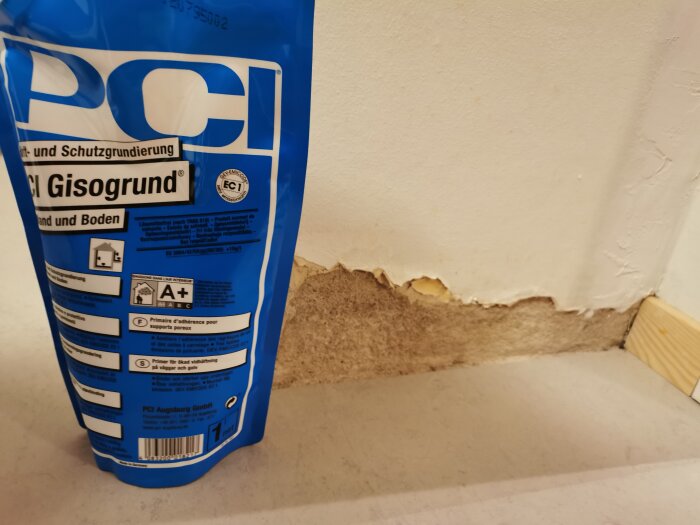 Blå förpackning varumärket PCI, skadad vit vägg, brun grund, byggmaterial, renoveringsprojekt.