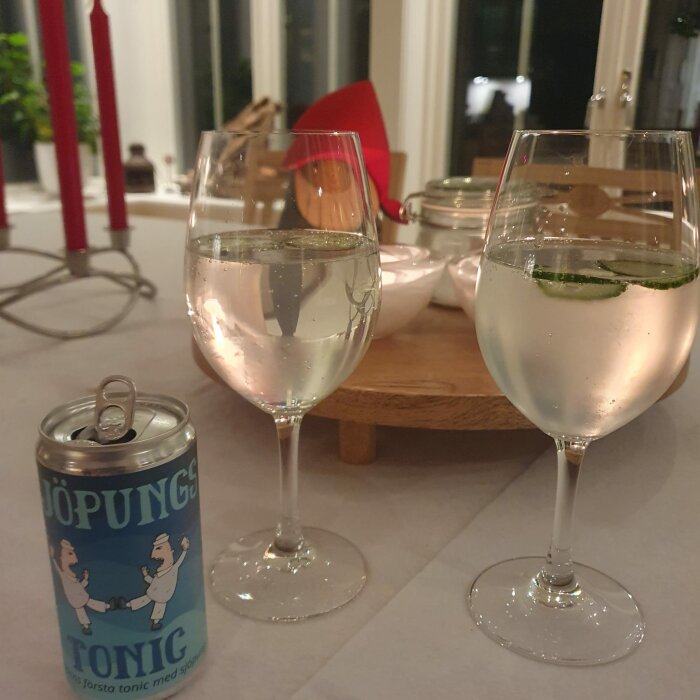 Två glas med bubblig dryck och lime, burk tonic, mysig bordsdukning, inomhusmiljö.