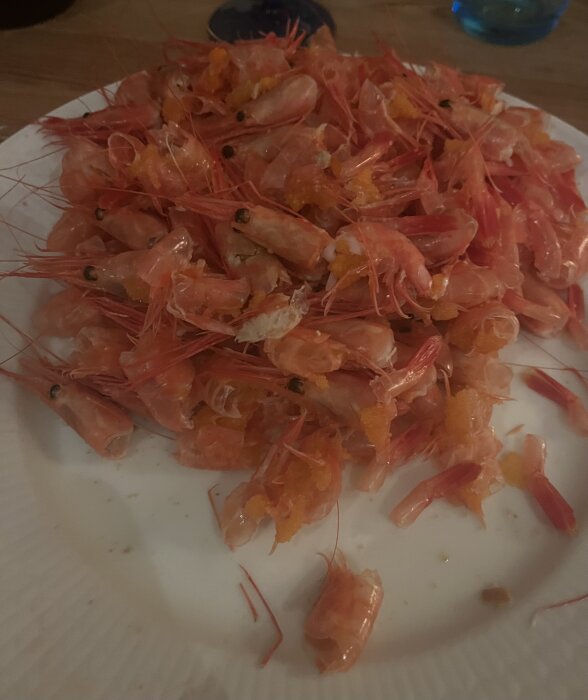 En tallrik med skalade räkor, skal och stjärtar utspridda, efter måltid, rosa och orange nyanser.