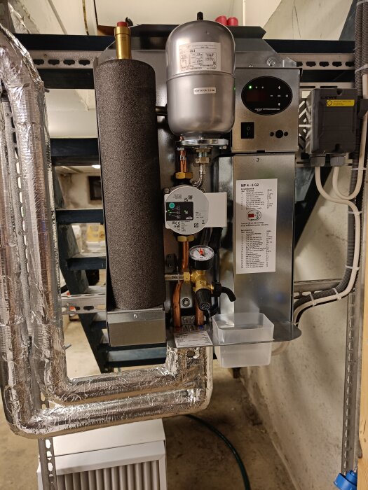 Värmesystemskomponenter installerade i källare: cirkulationspump, expansionskärl, filter, rör med isolering.