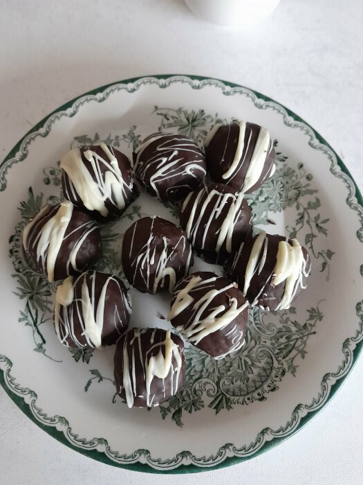 Chokladöverdragna bakverk med vit chokladdekor på ett mönstrat fat.