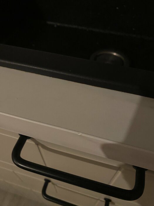 Närbild av en öppen kökslåda med svart handtag, vit front och mörk insida.