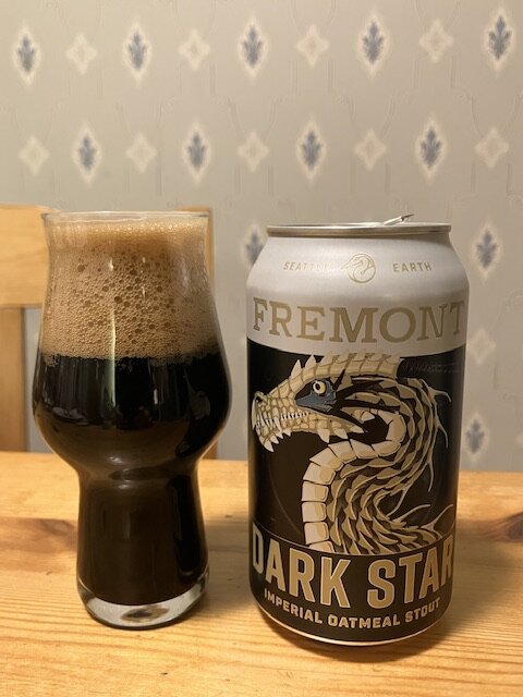 Ett glas mörkt öl bredvid en ölburk med texten "FREMONT DARK STAR", mönstrad tapet i bakgrunden.