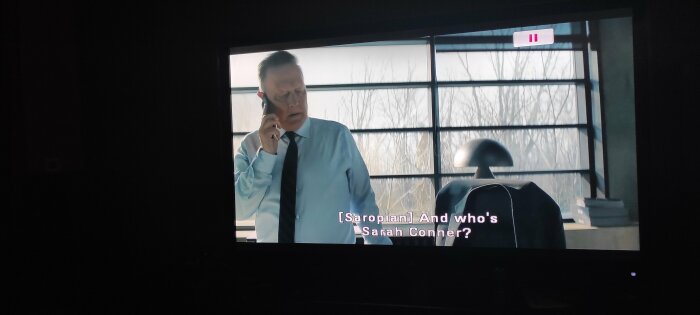 Man i skjorta och slips pratar i telefon, kontorsmiljö, textad dialog på skärm.