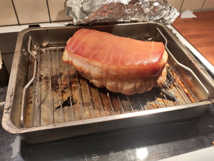 Rimmad julskinka på ugnsgaller, ofärdig, köksmiljö, foliebit i hörnet, förberedelse för griljering.