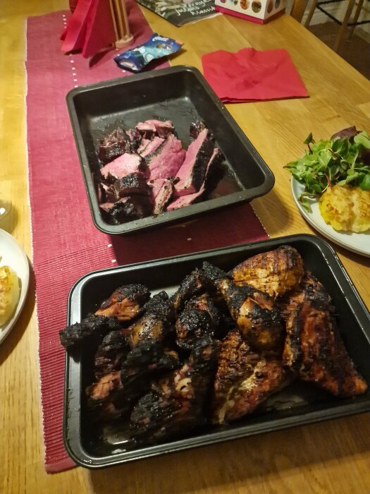 Två grillrätter på bordsduk. Stekt revben, något bränt, stekt kött i bakgrunden. Middagsatmosfär, sallad och potatisgratäng sidorätter.