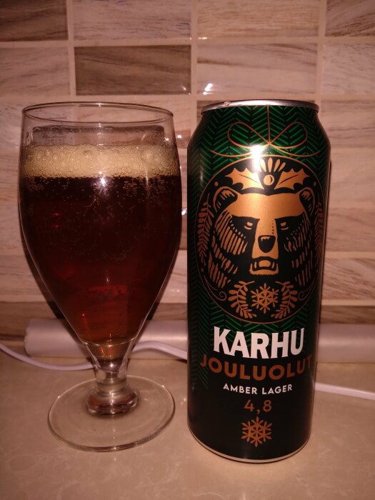 Ett glas med öl och en ölburk märkt "KARHU JOULUOLUT". Amber lager, juldesign, 4,8 % alkohol.