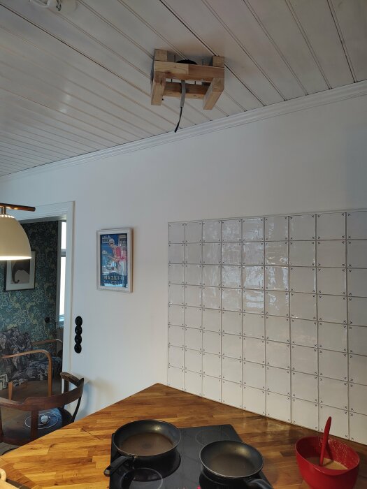 Ett kök med spis, taklampa, trästolar, spegel och hängande träkonstruktion från taket.