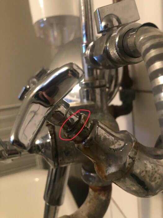 Bild på en duschblandare, kalkavlagringar synliga, rost nära röd ring, behöver rengöring och underhåll.