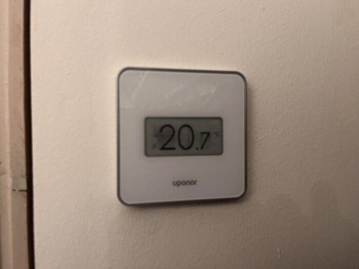 Digital termostat på vägg visar inomhustemperatur, 20.7 grader Celsius, varumärke Uponor, enkel design.