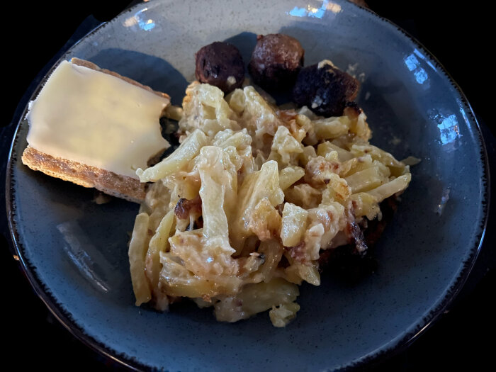 En tallrik med pasta, köttbullar och smält ost på bröd, serverad i mörk miljö.