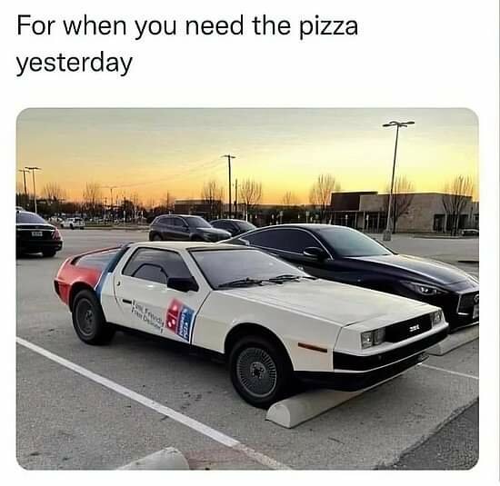 Bil parkerad med pizzaleverans paintjob, liknar en berömd filmbil, humoristisk skylt, parkeringsplats vid solnedgång.