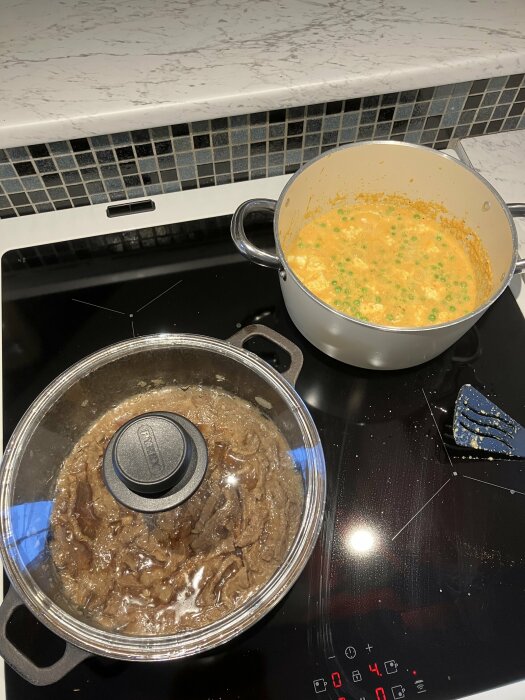 Två kastruller på spisen, en med sås och ärter, den andra med kött och lock. Induktionshäll i bakgrunden.