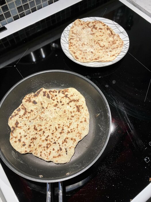 Stekpanna på spishäll med bröd, ett till på tallrik, smulor runtomkring.