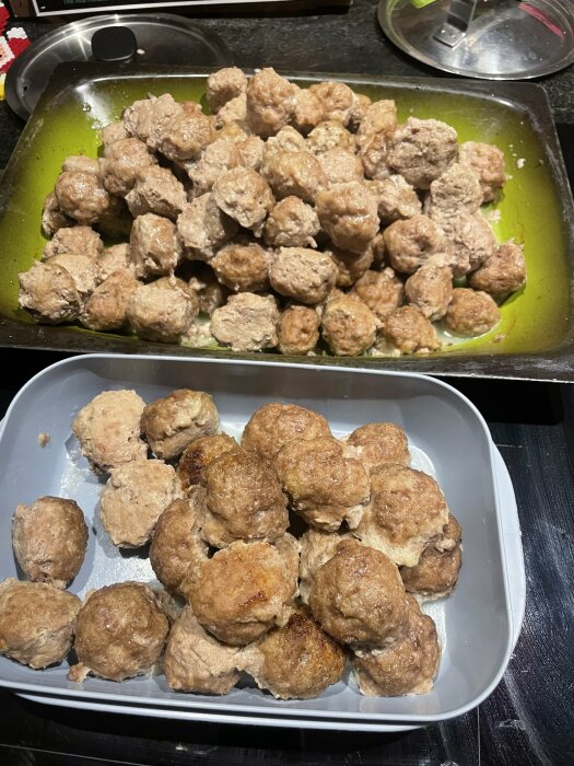 Två formar med stekta köttbullar, ena grön och andra grå, på köksbänk.