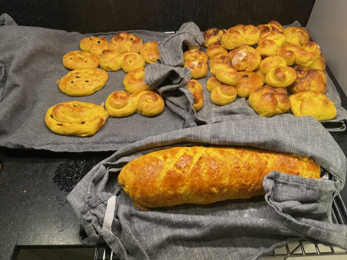 Nybakat bröd och bullar på grå kökshanddukar, hemmabak ser gott ut.