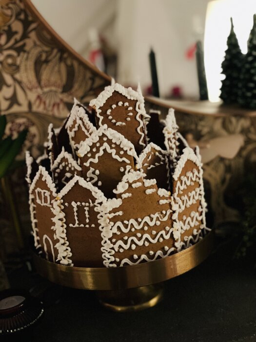 Pepparkakshus som formar en krona, på guldfärgad tallrik, juldekorationer i bakgrund, hemtrevligt och festligt.