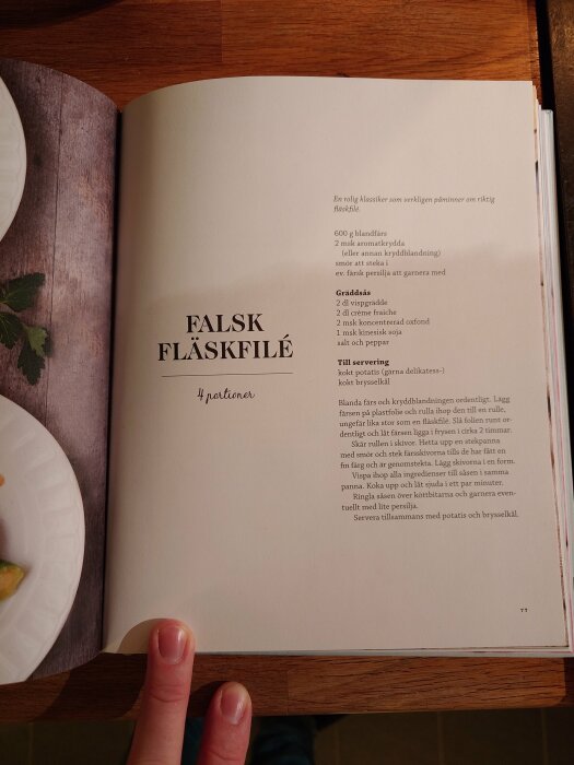 En öppen kokbok med recept för "Falsk fläskfilé" och ingredienslista, sidnummer 77, hand håller sidan.
