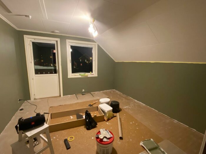 Ett oinrett rum under renovering med målarfärg och verktyg utspridda på golvet.