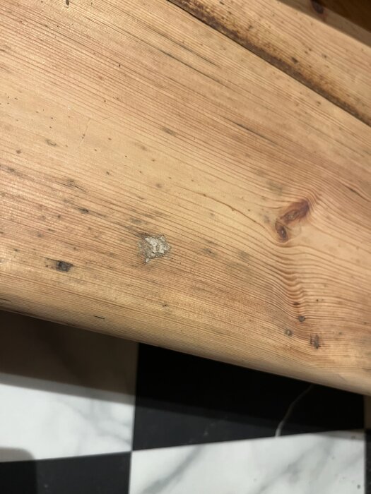 Träyta med knutar och skador, svartvitt marmorgolv synligt nedtill.